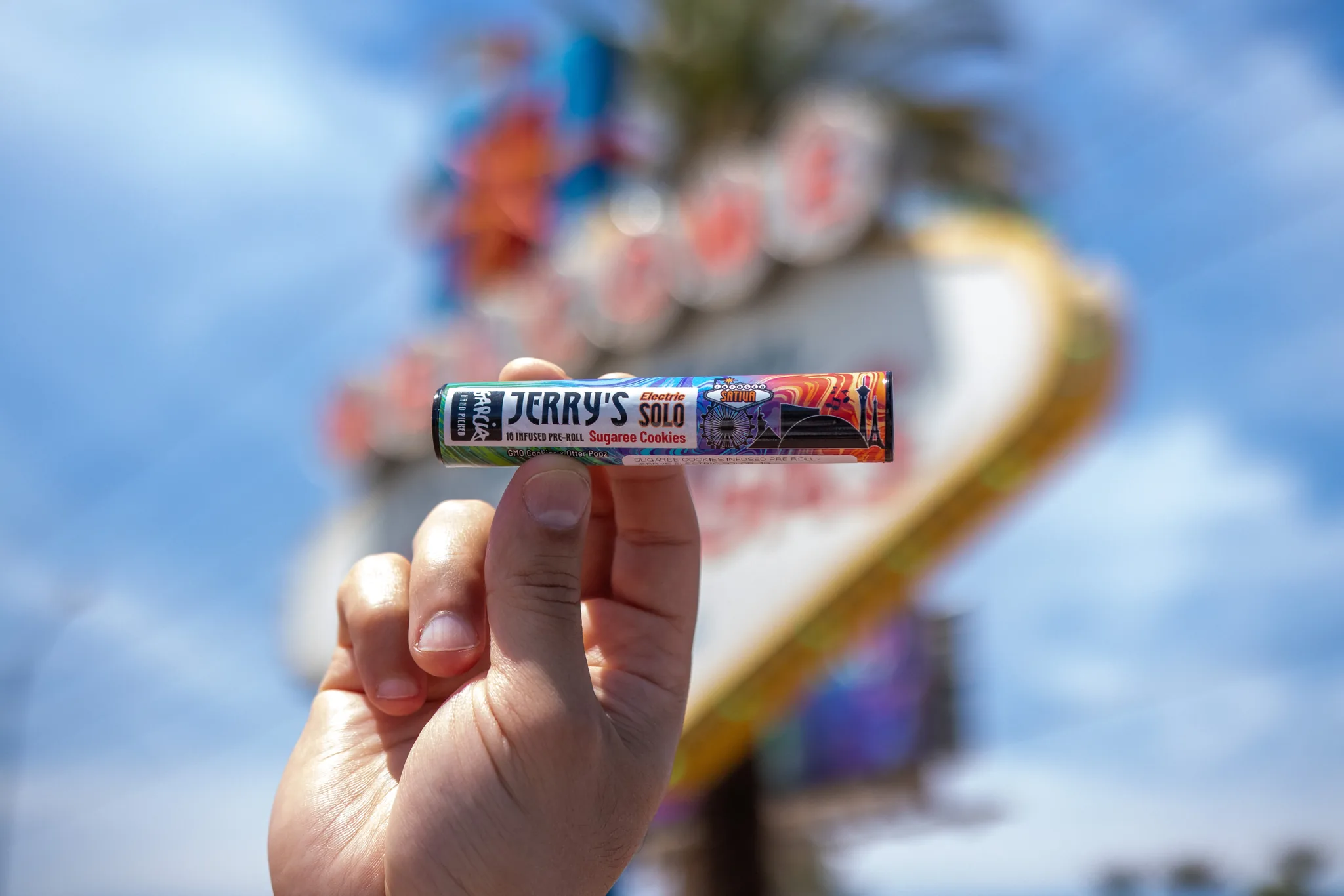 A hand holding a Garcia Hand Picked Jerry's Solo infused pre-roll tube in front of the Welcome to Fabulous Las Vegas sign